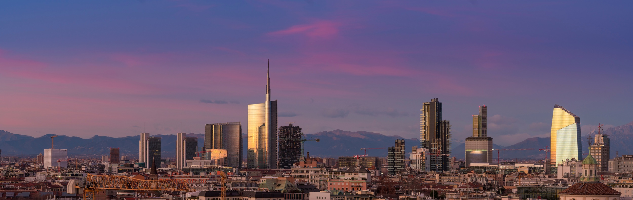 Aerial view of Milan skyline at sunset with alps mountains in the background.