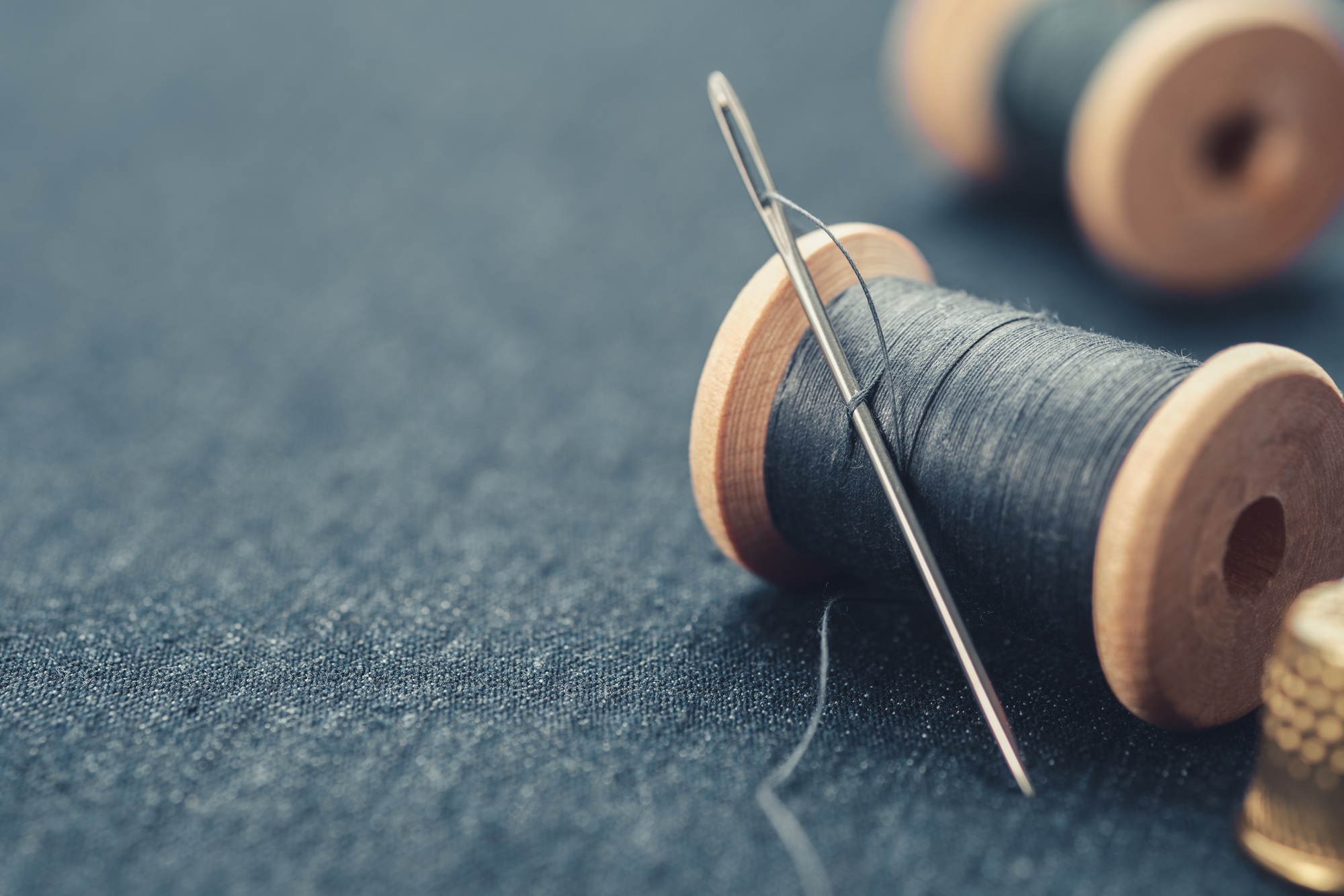 Wooden spools of blue thread and thimble on blue jeans cloth.